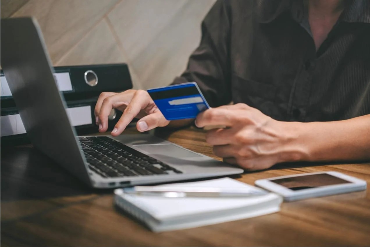 Person sitting at desk making a purchase at their computer with credit card in hand.