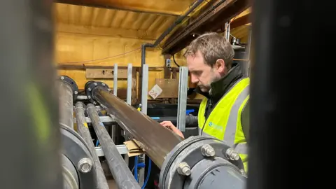 Professor Bell looks at a pipe carrying water into the facility in Weymouth. He is wearing a hi-vis jacket.  