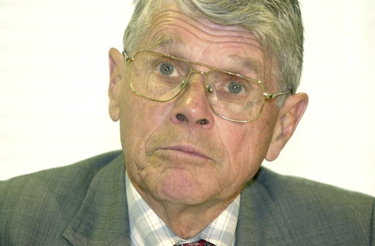 Grey haired man wearing checked shirt and grey jacket