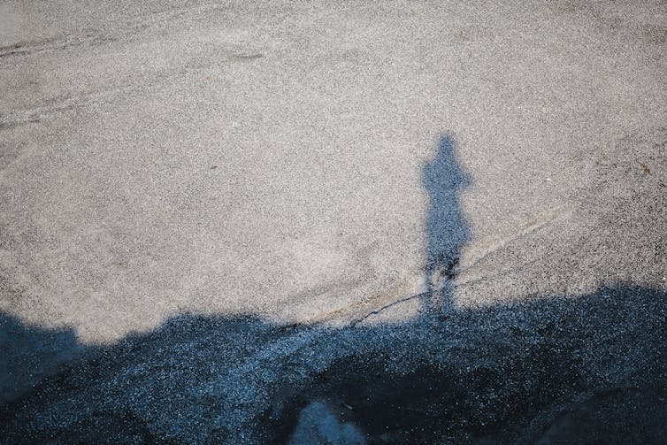 The shadow of a small figure on grey pavement.