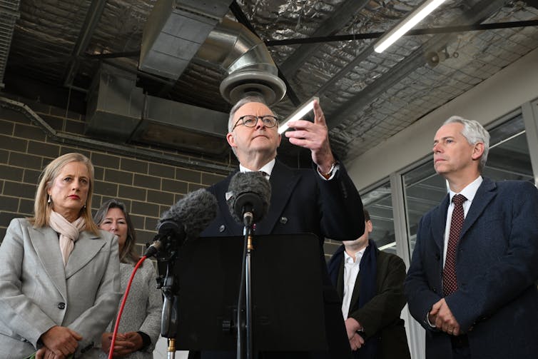 A man speaking into a microphone beneath a vent.
