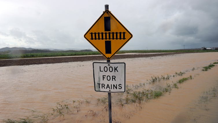 A rail crossing sign reading'Look for trains' in front of a flooded train line.