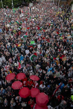 Aerial photo of a large crowd with a cluster of red umbrellas in the foreground.