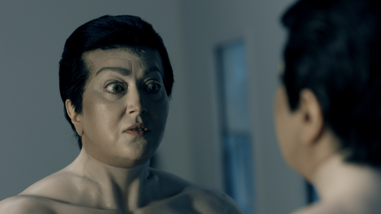 A weird looking man looks into a mirror.