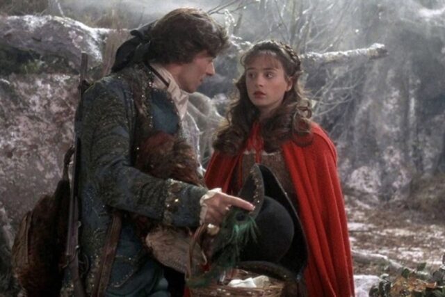 beautiful young dark-haired girl in a red hooded cape talking to a darkly handsome young man with a rakish look about him
