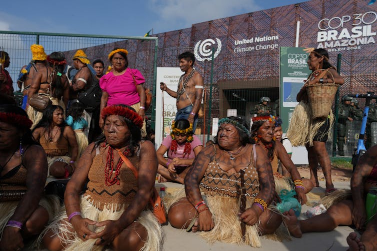 A group of Indigenous people sit on the ground to block access to the UN climate summit.