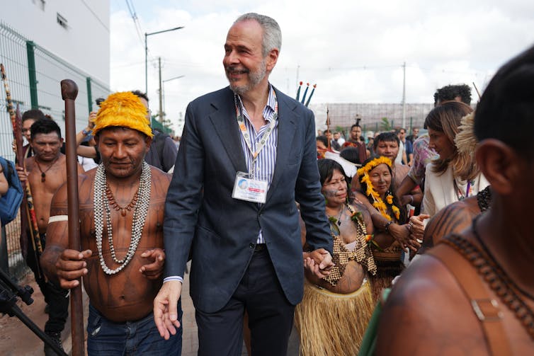 COP30 president André Corrêa do Lago walks through a group of Indigenous people and holds the hand of one woman.