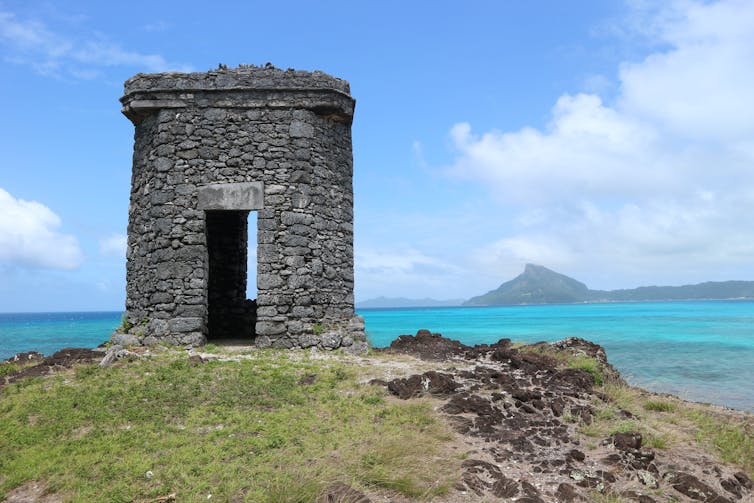 A watch tower built on a slight hill overlooking a turquoise lagoon.