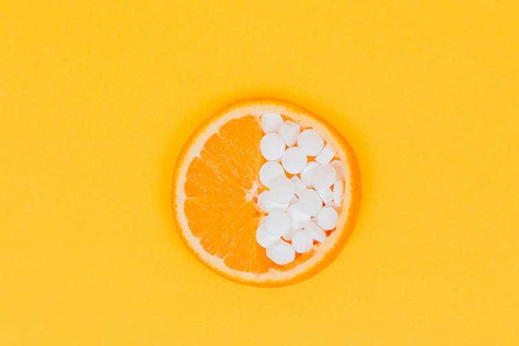 An orange with half holding vitamin C tablets