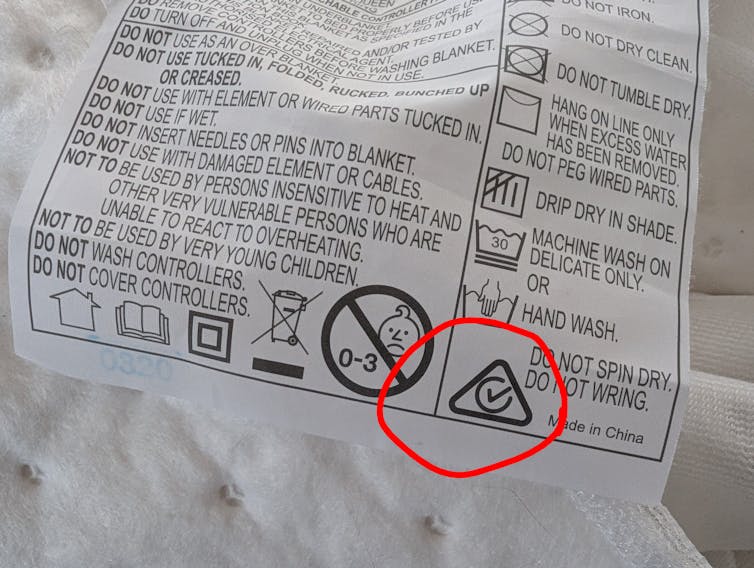 A blanket tag with safety instructions and a tickmark in a triangle circled in red.