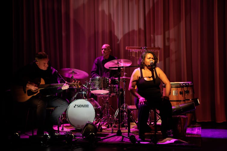A woman sings onstage while a band plays alongside her.