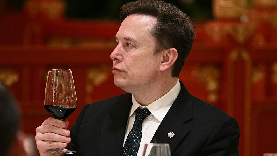 Musk, wearing a black suit, white shirt and black and white dotted tie, holds a glass of red wine while at an event in Beijing, during a recent US trade visit.