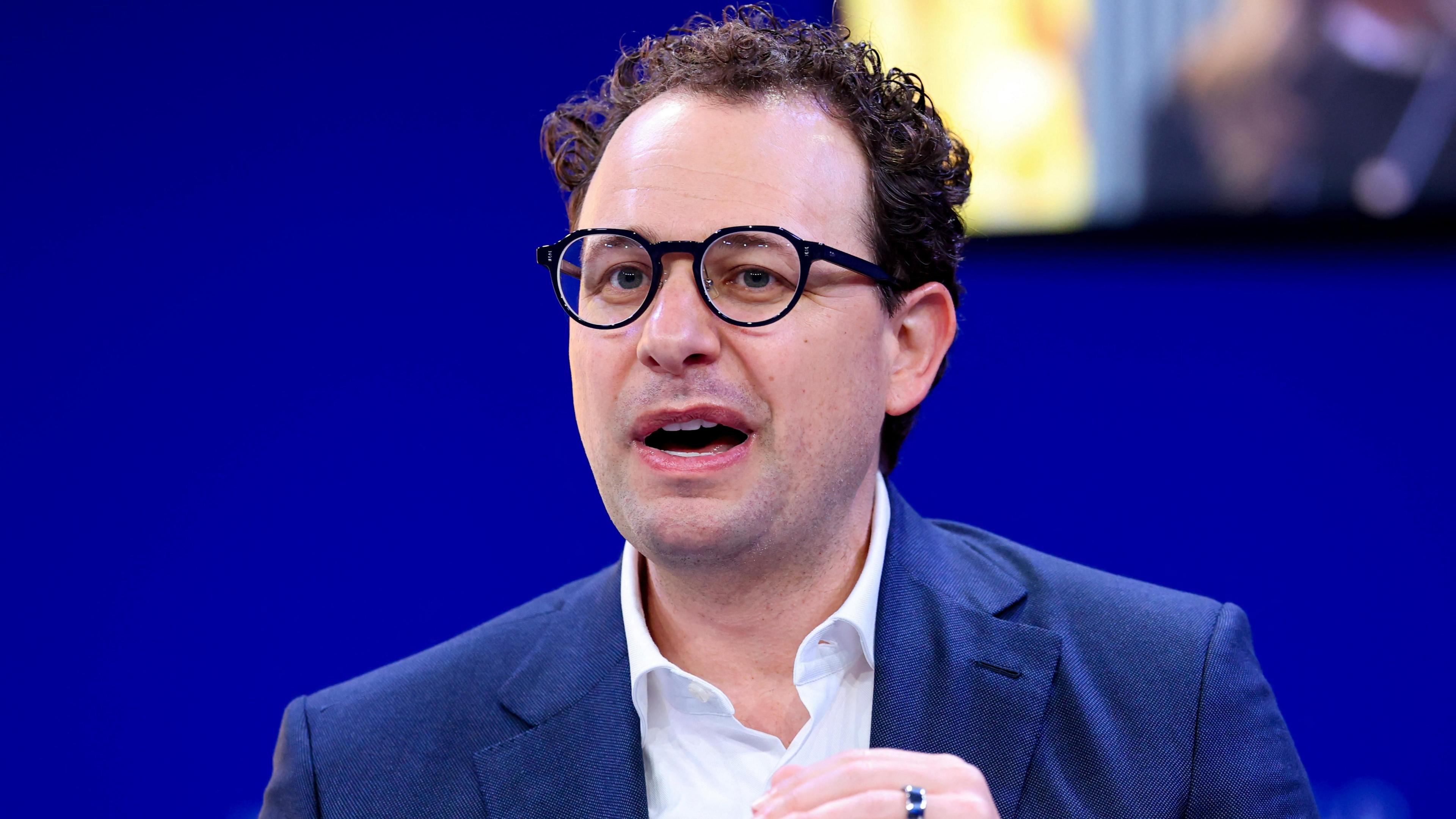 Anthropic CEO Dario Amodei speaking on a stage while gesturing with his hands.