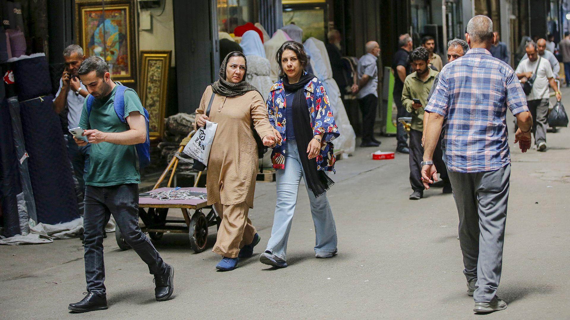 Several people walk on the streets of Tehran on a shaded street in July.