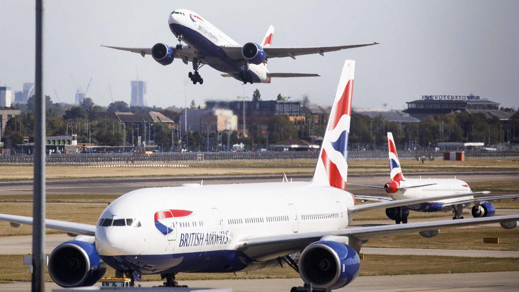 Three British Airways aircraft at Heathrow Airport, one is taking off in the distance with London skyline in the background