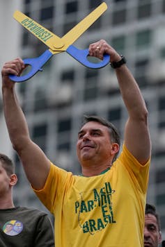 Opposition presidential candidate Flavio Bolsonaro holds up a pair of symbolic scissors with the word tesourão, Portuguese for'big scissors'.