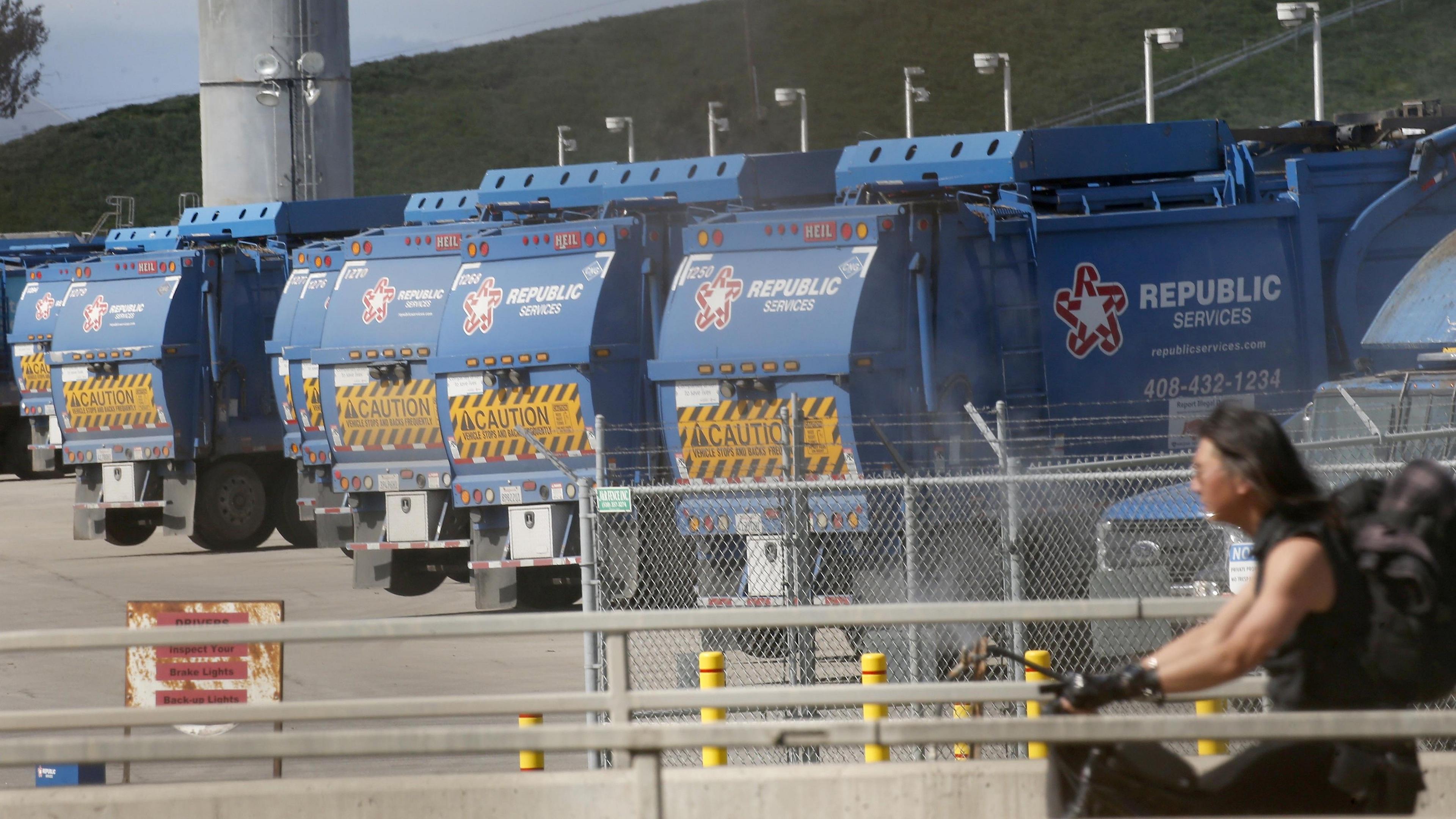 Blue rubbish trucks lined up at Newby Island landfill. A cyclist is in the foreground.